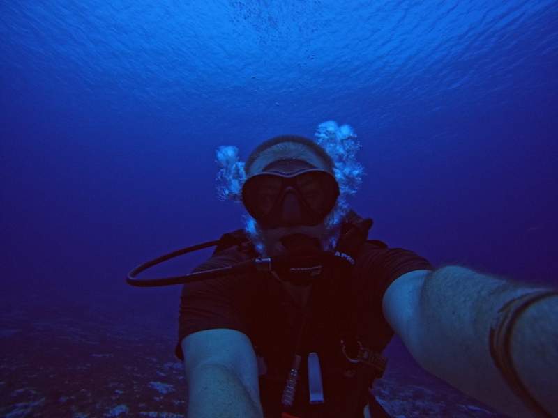 A scuba diver in deep blue water, with a stream of bubbles rising toward the surface.