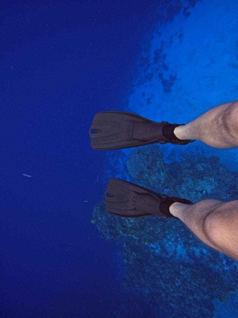 A scuba diver swimming away through deep blue water.
