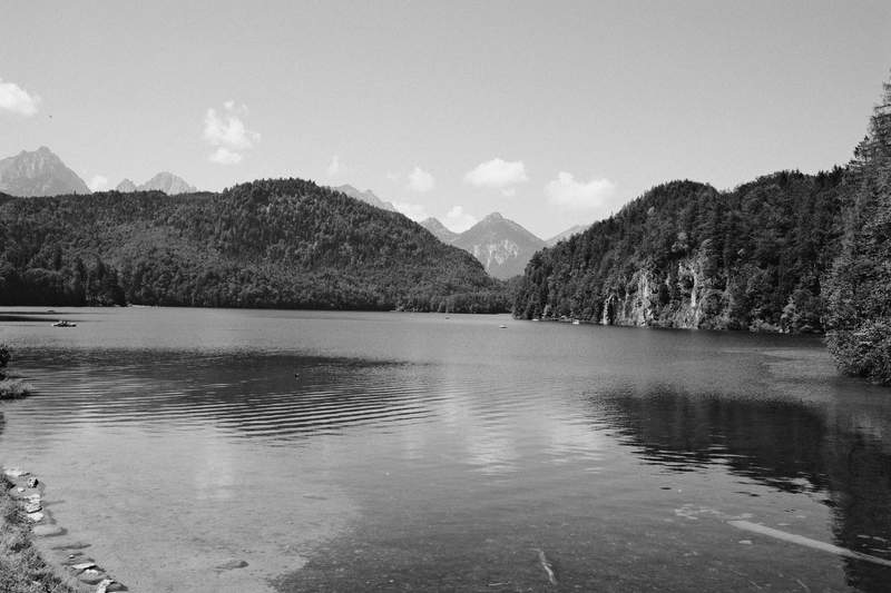 Alpsee in the foreground, Hohenschwangau Castle on a wooded hill, and the Alps behind.