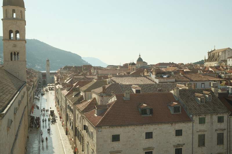A stone lane in Dubrovnik with cafe umbrellas, opening toward the walls and the sea.