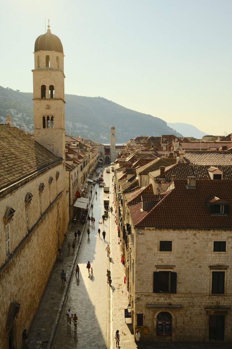 A stone passage in Dubrovnik opening onto a small square of red-roofed buildings.