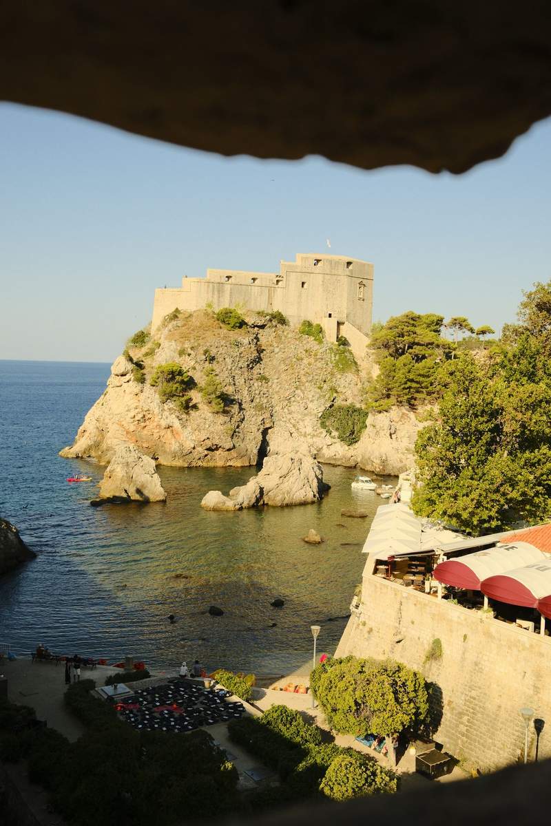 A walled lane in Dubrovnik leading down to a stone tower and the sea.