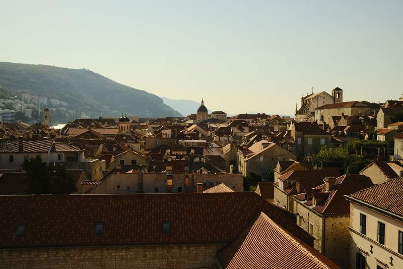 Dubrovnik's old town at golden hour, red roofs packed down to the harbor and an island offshore.