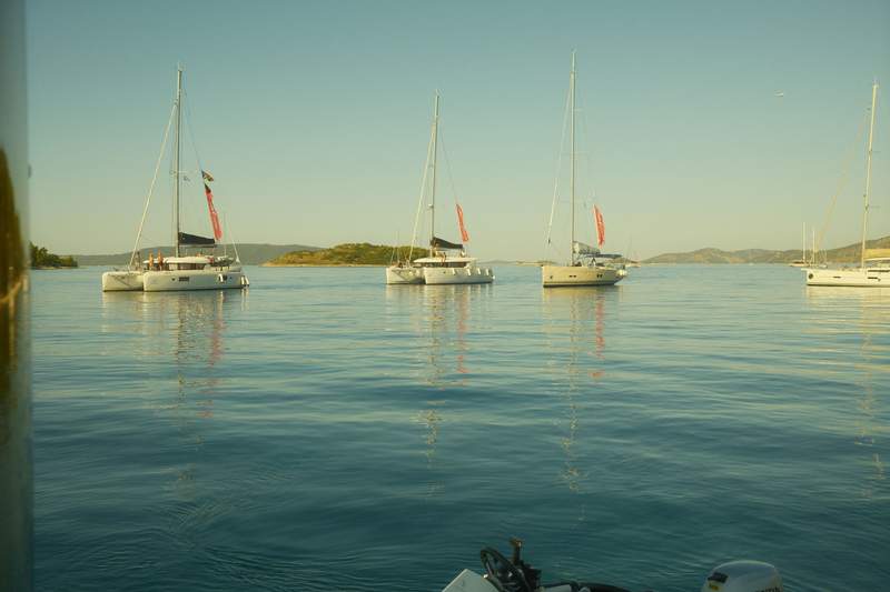 The bow of a catamaran on turquoise water, with rocky islands ahead.