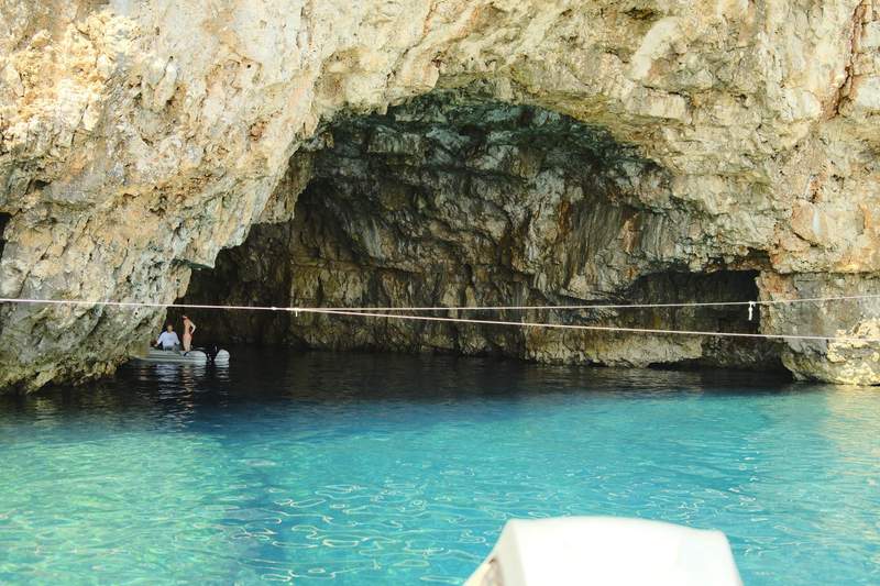 Inside a sea cave on Vis, looking out at bright turquoise water and a pale rock island.