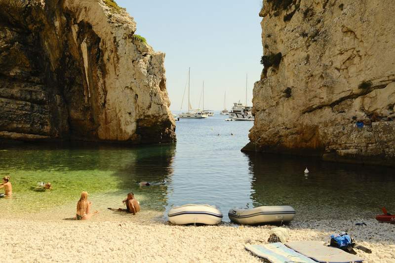 People swimming in clear turquoise water at the base of a rocky cliff on Vis.